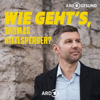 Thomas Hitzlsperger blickt in einem hellen Sakko vor einer steinernen Felswand in die Ferne.